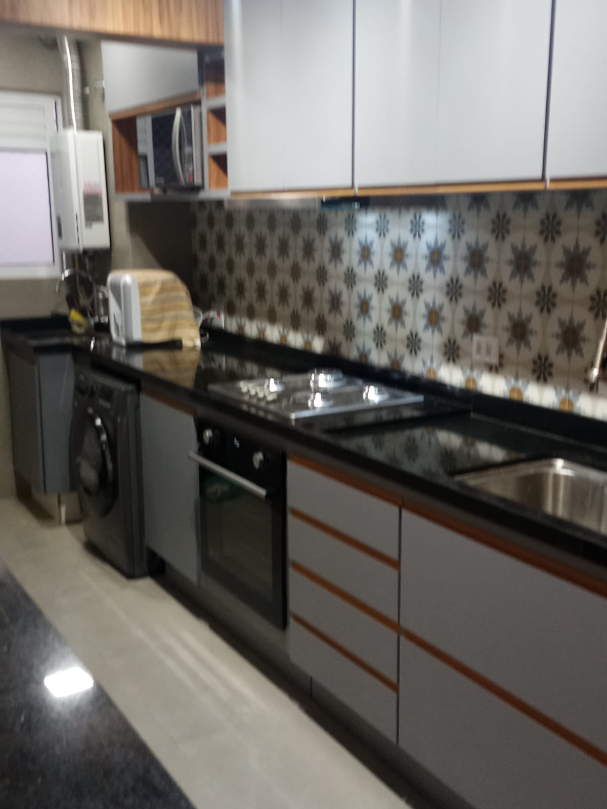 Cozinha planejada com armários cinza, detalhes em madeira, bancada de granito e backsplash estampado.