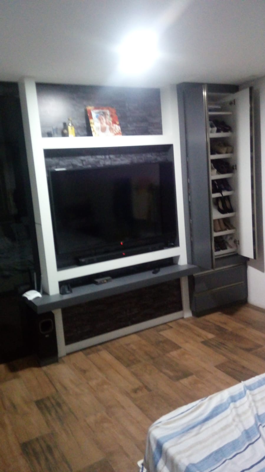 Painel sob medida para quarto com TV embutida, prateleiras decorativas e sapateira lateral integrada.